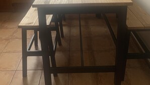 Une table en bois, dotée d’un cadre en métal, se trouve dans une pièce aux murs en bois et à la grande fenêtre donnant sur un paysage montagneux.