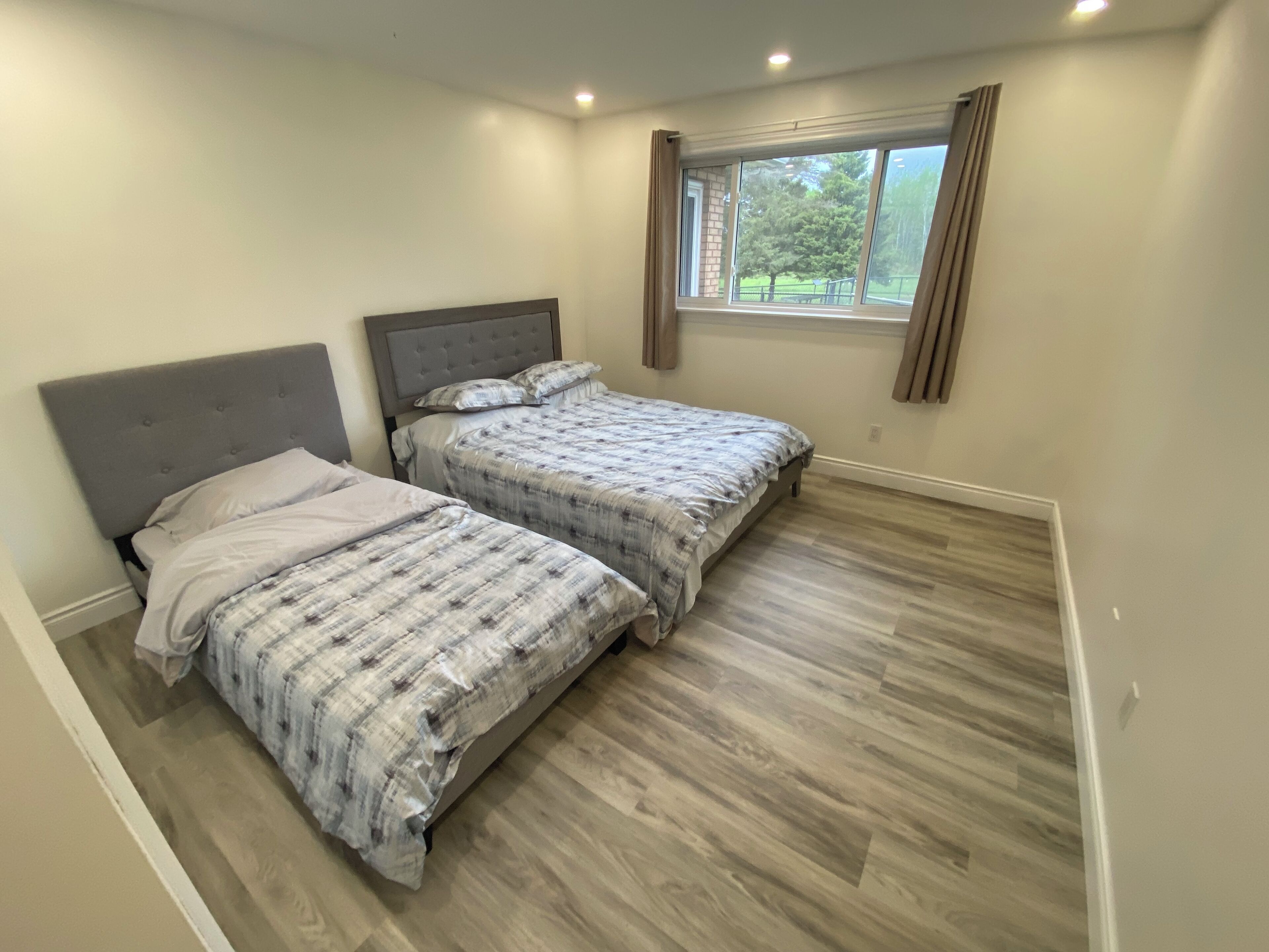 A bedroom with two beds, a window with curtains, and a wooden floor.