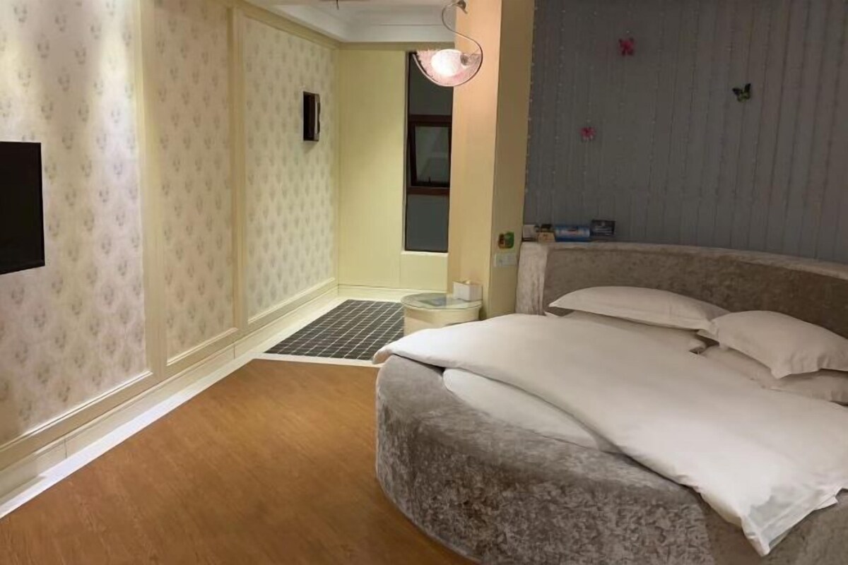 Un dormitorio con cama, mesita de noche, televisor de pared y ventana.