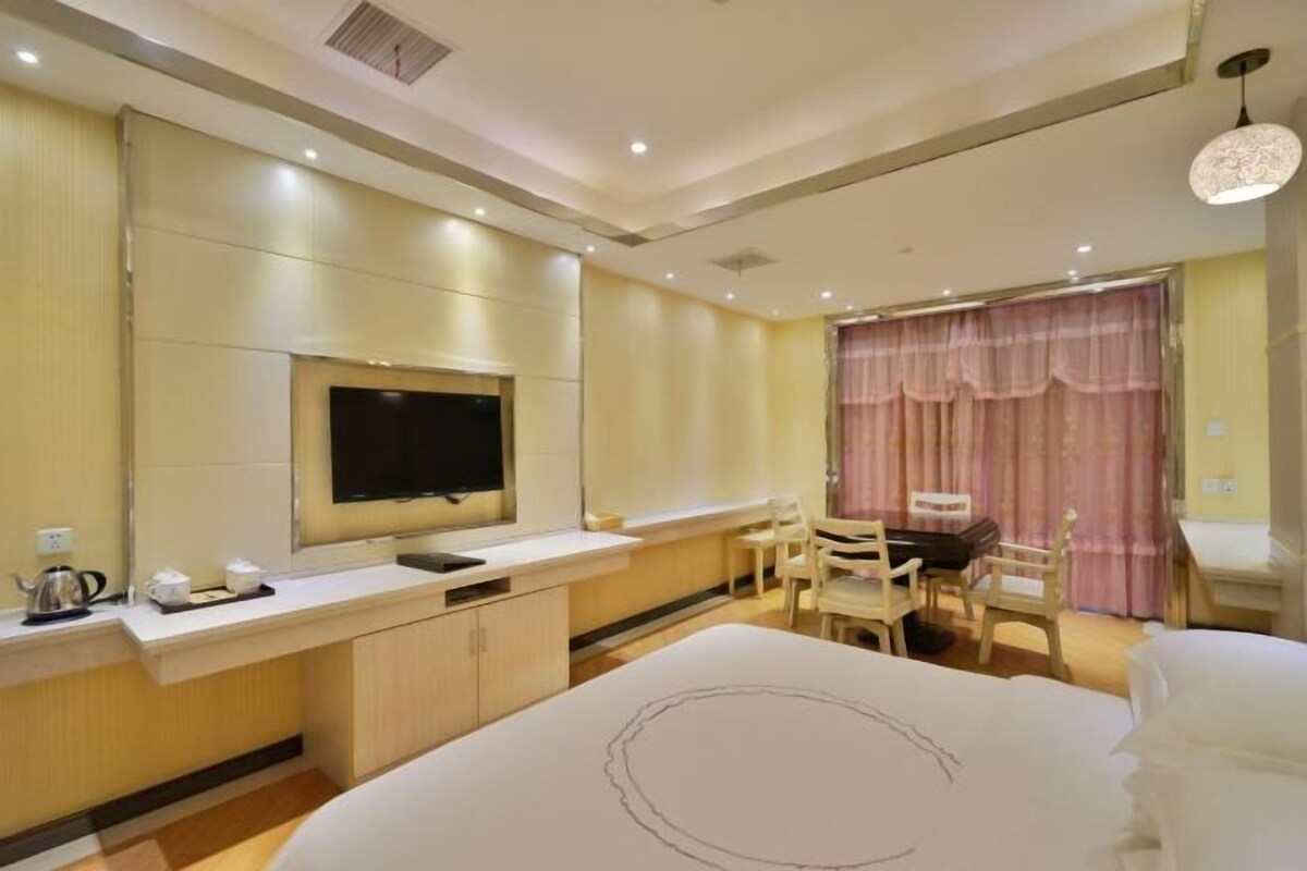 A hotel room with a bed, a desk, a chair, a television, and a window with curtains.