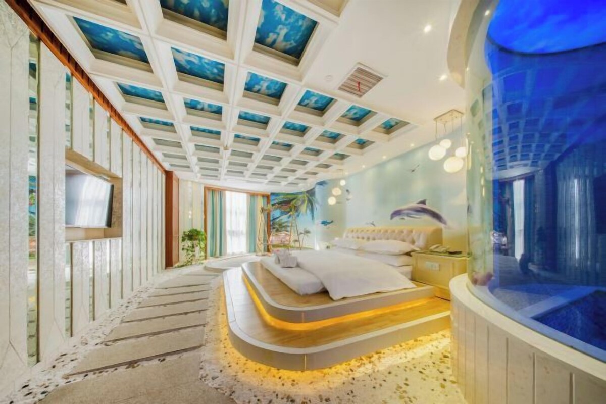 A modern bedroom with a unique ceiling design, a large bed, and a view of the ocean through a glass wall.