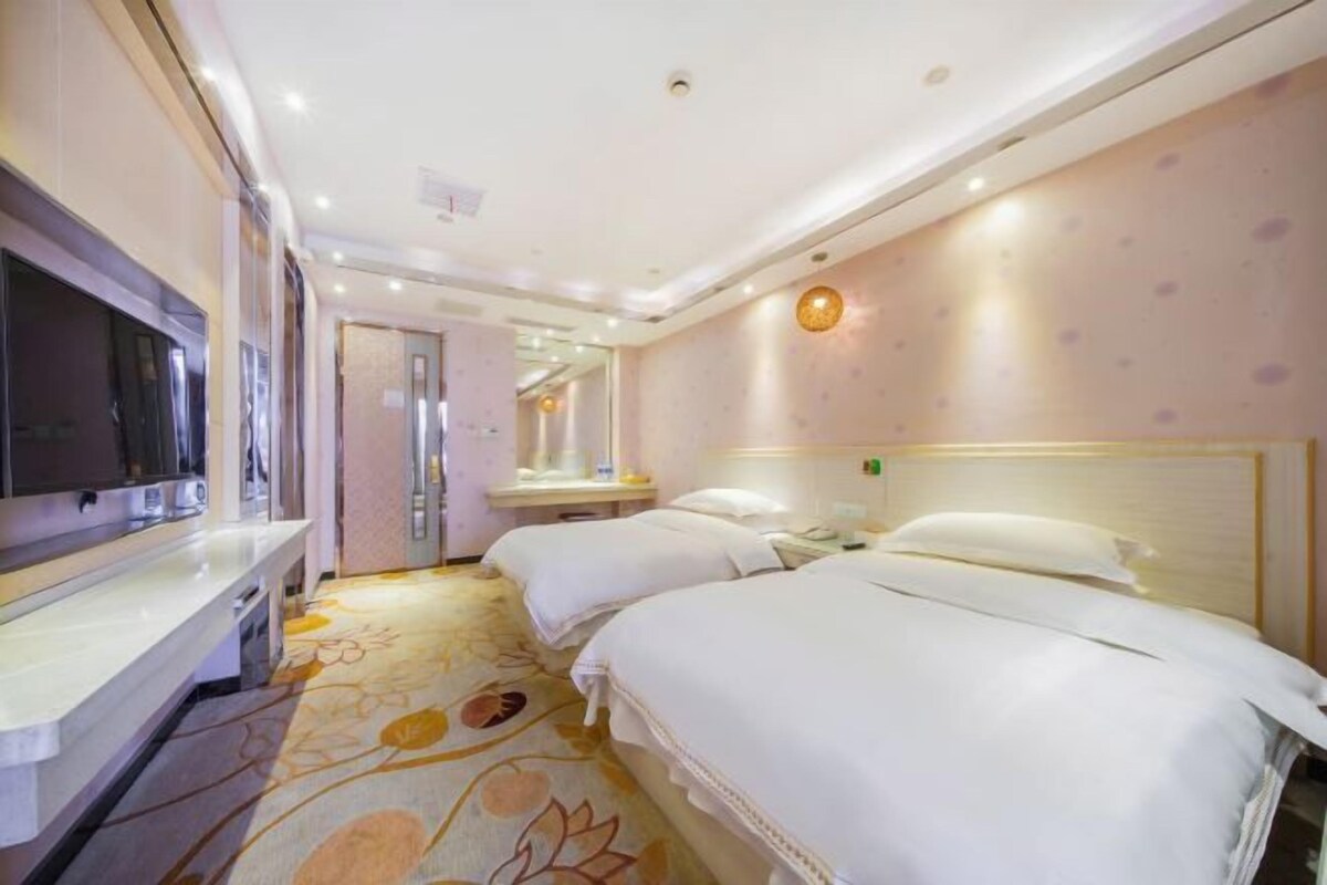 A hotel room with two beds, a TV, a mirror, and a floral carpet.