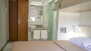 Habitació d'hotel amb un llit, un bany amb un lavabo i tovalloles, i una porta que condueix a una altra habitació.