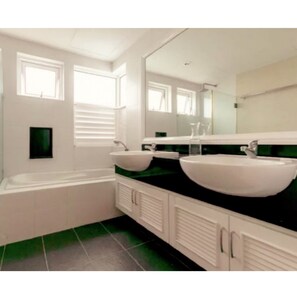 A modern bathroom with a bathtub, two sinks, and a large mirror.