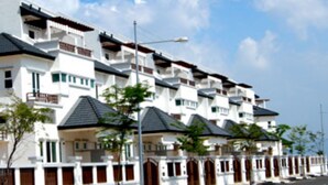 A row of modern, multi-story residential buildings with balconies, a clear sky, and a paved road with a curb. - HomeStay Nimah Seaview (George Town)