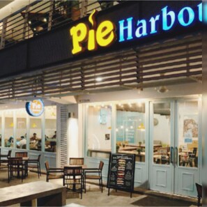 Ein Außenbereich mit Tischen und Stühlen, ein Schild mit der Aufschrift 'Pie Harbor' und eine Speisekarte vor dem Gebäude.