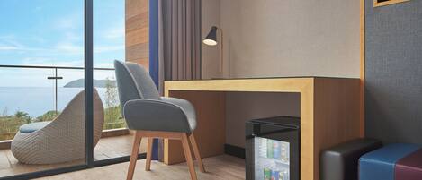 Una habitación moderna con un amplio ventanal, un escritorio, una silla, un cesto de basura pequeño y un sofá.