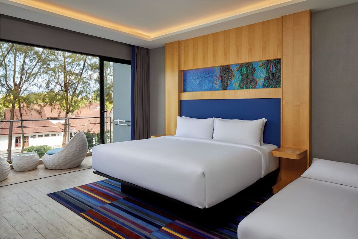 Une chambre d’hôtel moderne avec un grand lit, une vue sur l’extérieur et une peinture abstraite aux couleurs vives accrochée au mur.