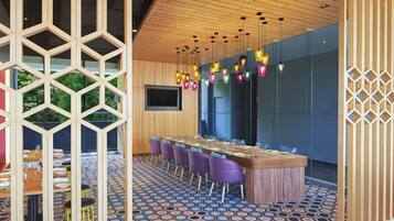 A modern dining area with a long wooden table, purple chairs, and colorful hanging lights.