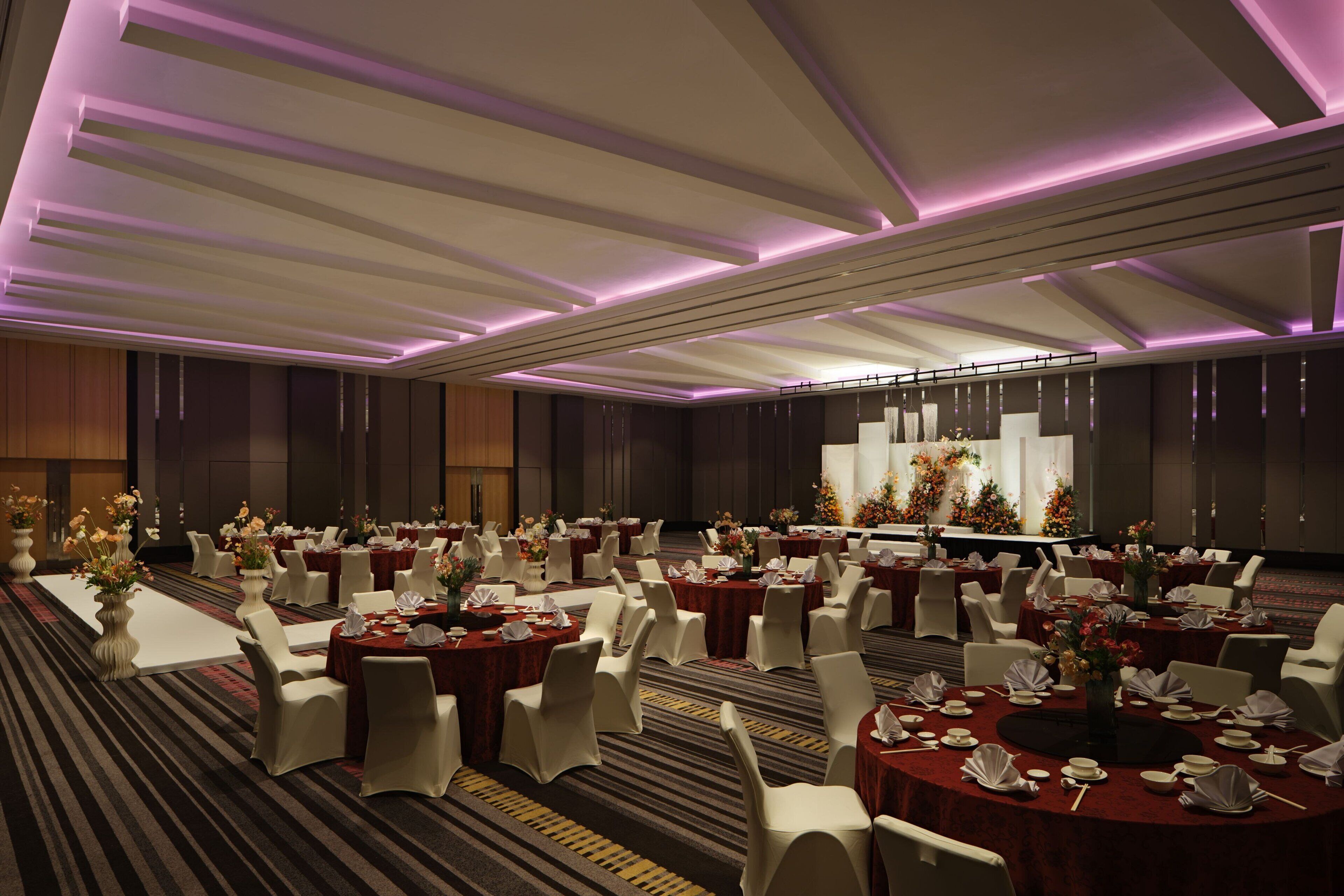 A banquet hall with round tables, white chairs, and purple lighting.