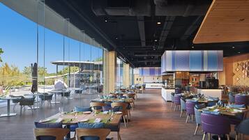 A spacious restaurant with long tables and chairs, large windows, and a view of the outdoors.