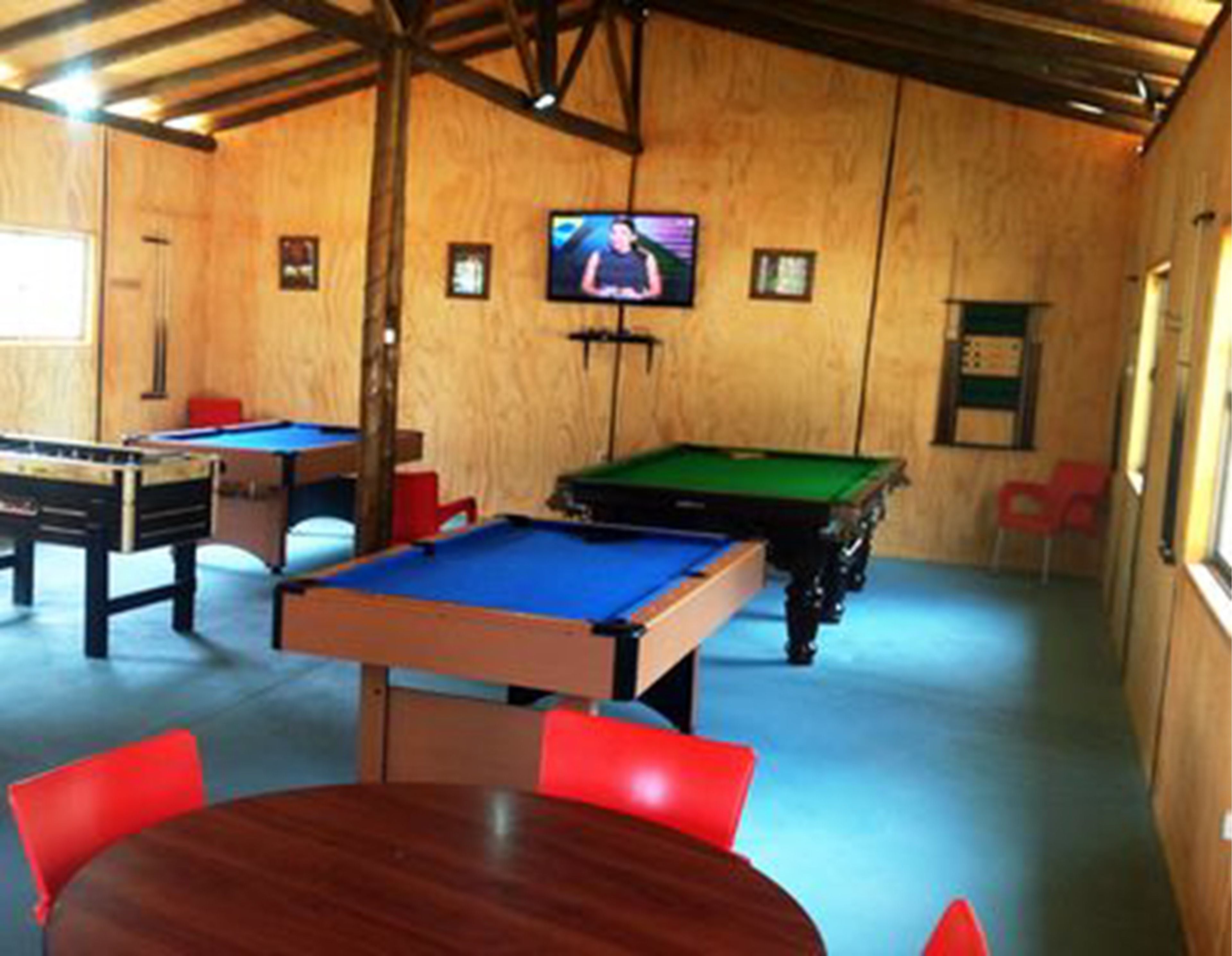 A room with a pool table, a foosball table, and a billiards table. There is a television mounted on the wall.