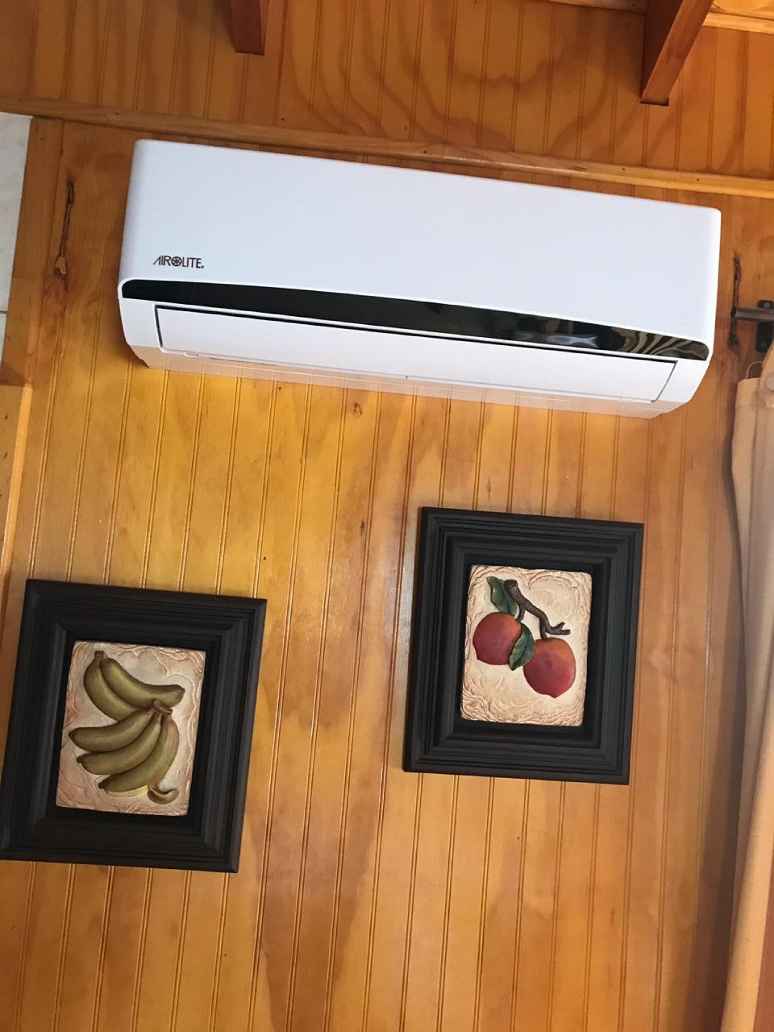 Een airconditioner bevestigd aan een houten muur, met daaronder twee ingelijste foto's.
