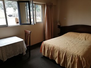 Una habitación de hotel con cama, mesa, silla, ventana con cortinas y lámpara.