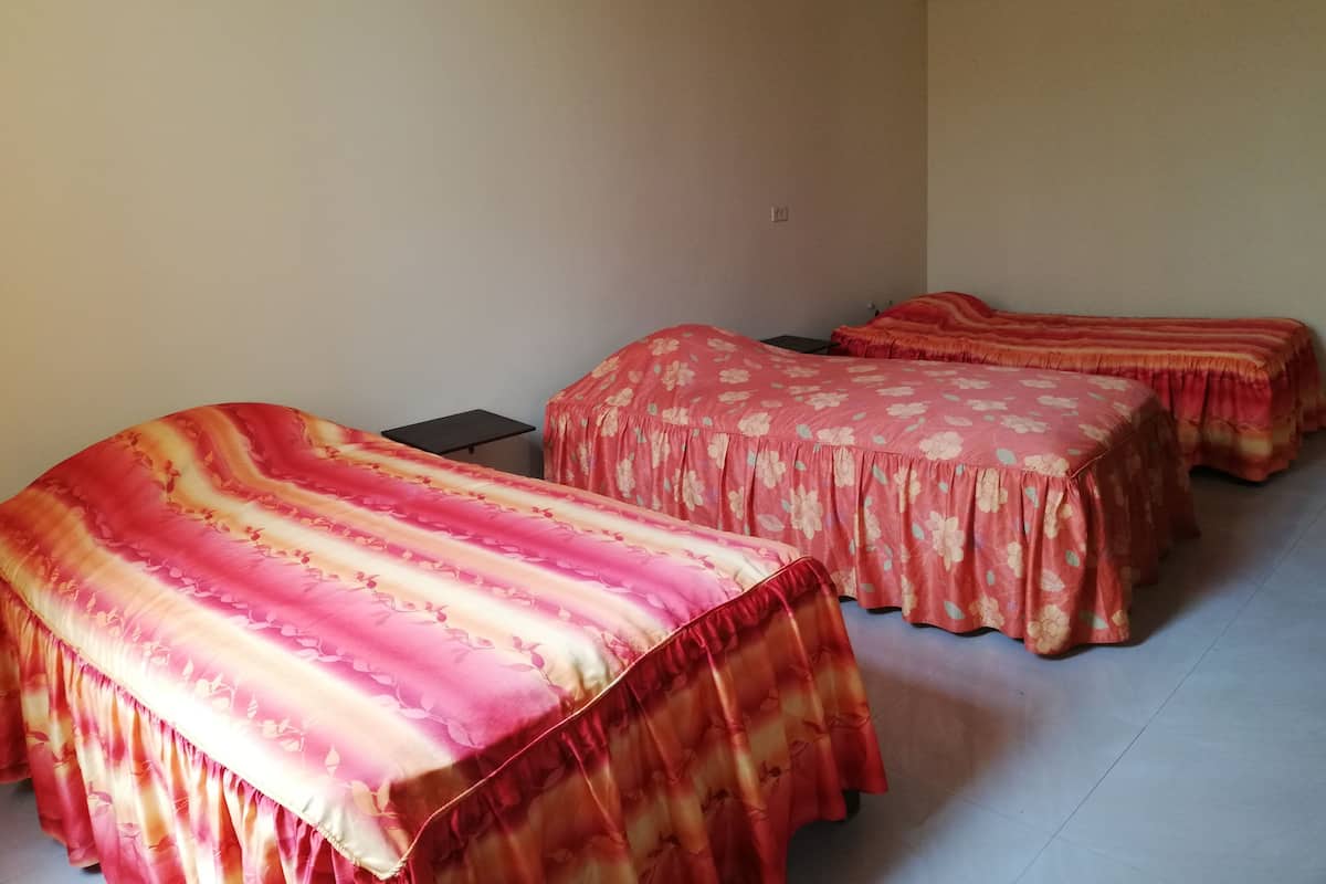 A room with two beds covered in floral-patterned bedding, a small table, and a plain wall.