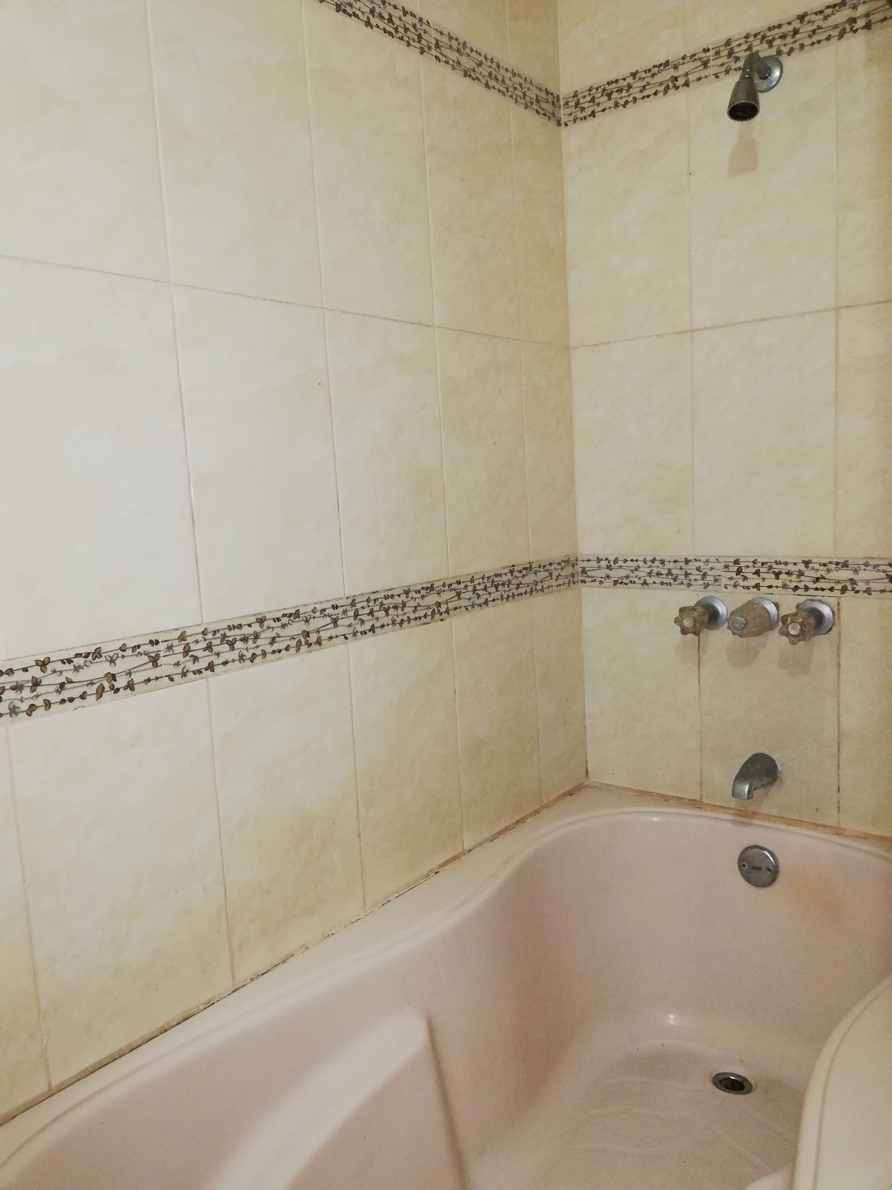 Een badkamer met een badkuip, betegelde wanden en een douchekop.