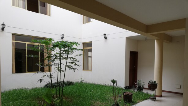 A courtyard with potted plants, a tiled floor, and a building with windows and a door. - La Quinta de Allison Hotel & Backpackers (Lima)