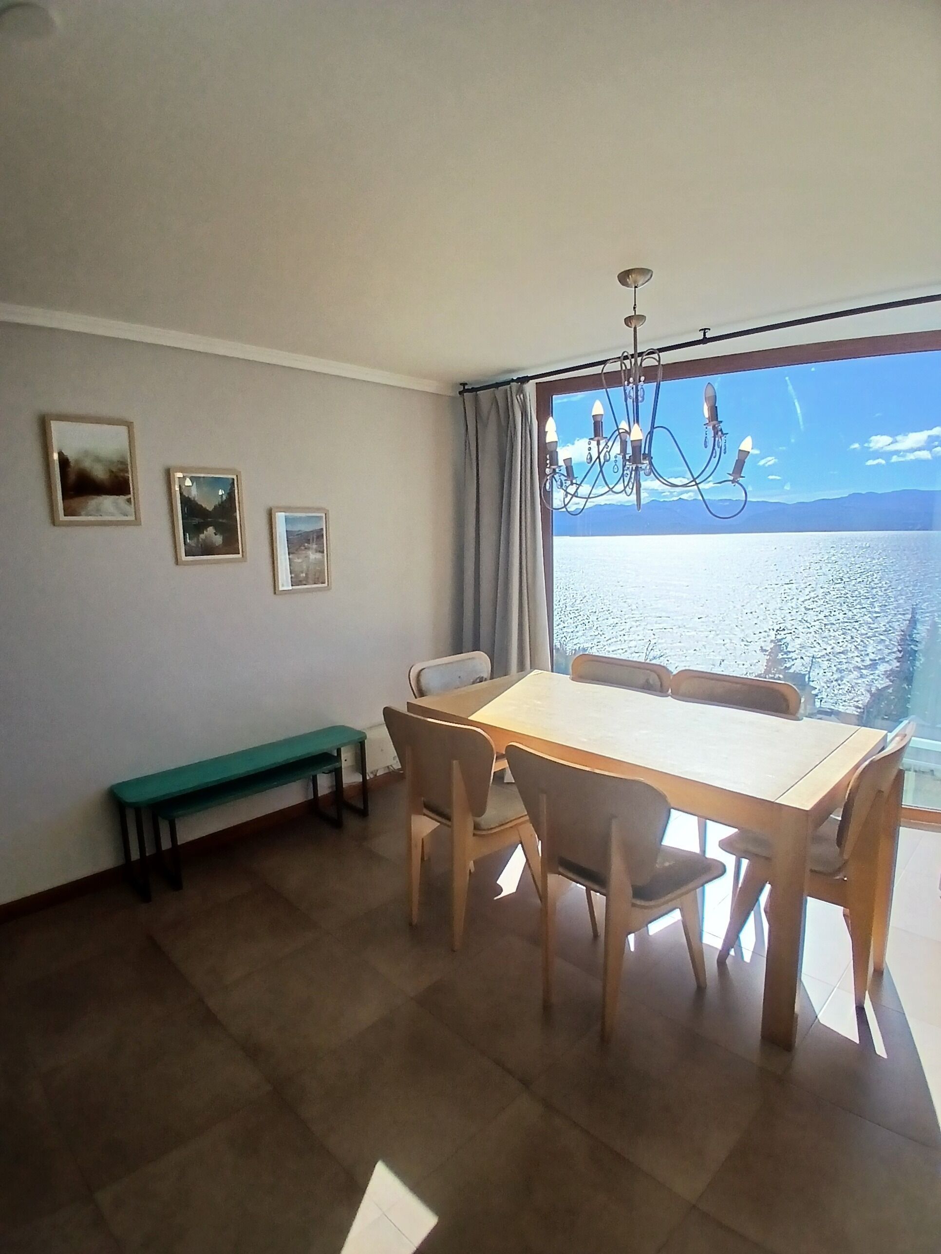 A dining area with a table and chairs, a bench, a chandelier, and a view of the sea.