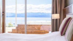 A hotel room with a large bed, a view of the sea, and a balcony with wooden steps. - Apartments Bariloche - Luxury Lake Views (San Carlos de Bariloche)