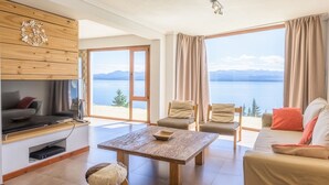 A spacious living area with a large window offering a view of a lake and mountains. - Apartments Bariloche - Luxury Lake Views (San Carlos de Bariloche)