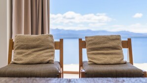 Two wooden chairs with beige cushions facing a large window overlooking a body of water and distant mountains. - Apartments Bariloche - Luxury Lake Views (San Carlos de Bariloche)