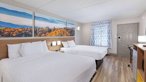 Hotellihuone, jossa on kaksi sänkyä, puinen pääty, syksyistä lehtikuviota esittävä taulu, kuvioitu verho ja pieni työpöytä, jossa on lamppu.
