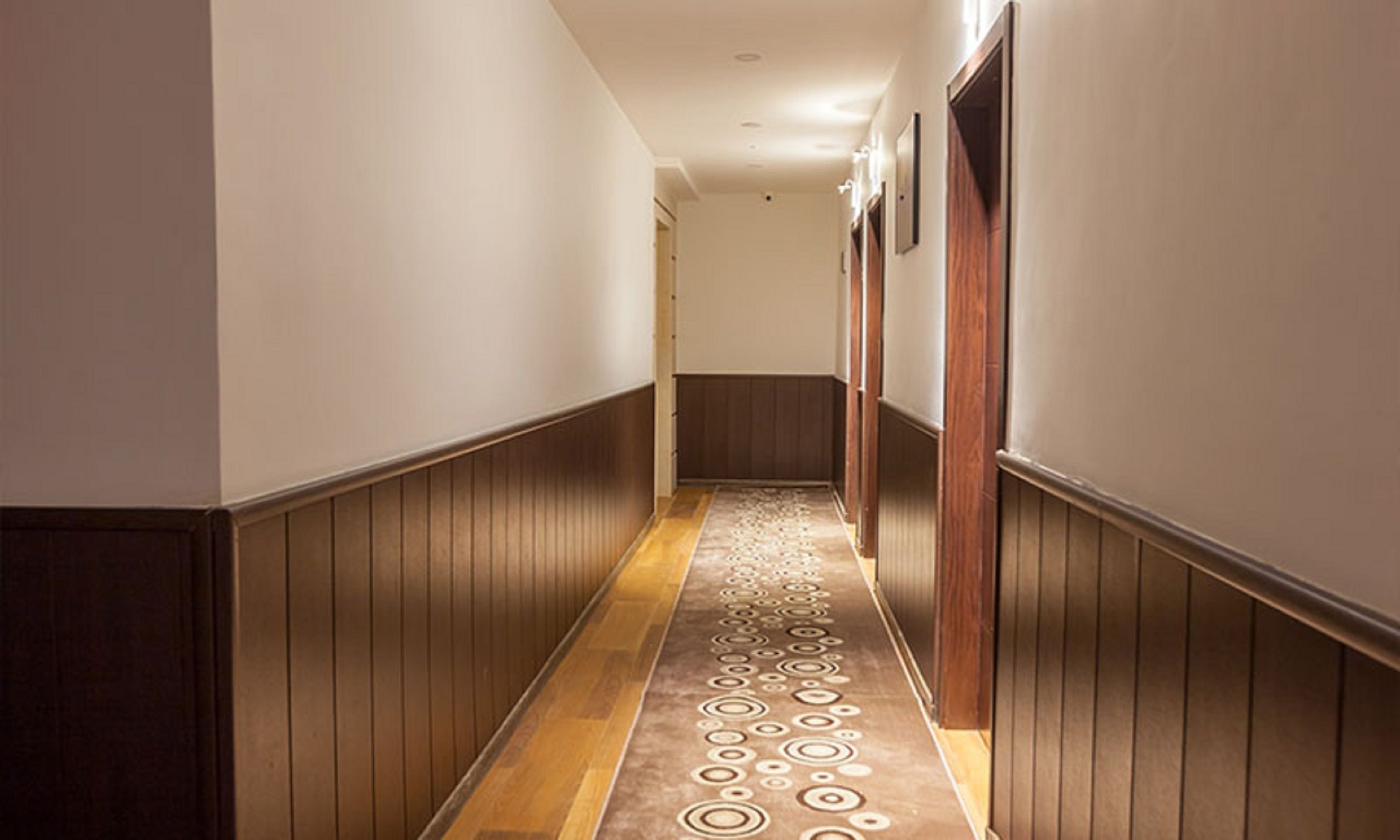 Un pasillo con paneles de madera, alfombra estampada e iluminación empotrada en el techo.