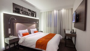 Una habitació d'hotel amb un llit gran, una taula de treball, una cadira, un televisor i un telèfon.