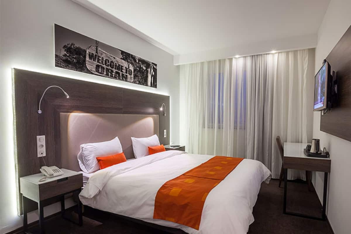 A hotel room with a large bed, a desk, a chair, a TV, and a telephone.