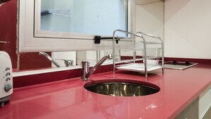 Eine Küche mit roter Arbeitsplatte, Spüle aus Edelstahl und einem Fenster darüber.