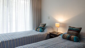 Hotellihuone, jossa on kaksi sänkyä, yöpöytä, lamppu ja ikkuna, jossa on verhot.