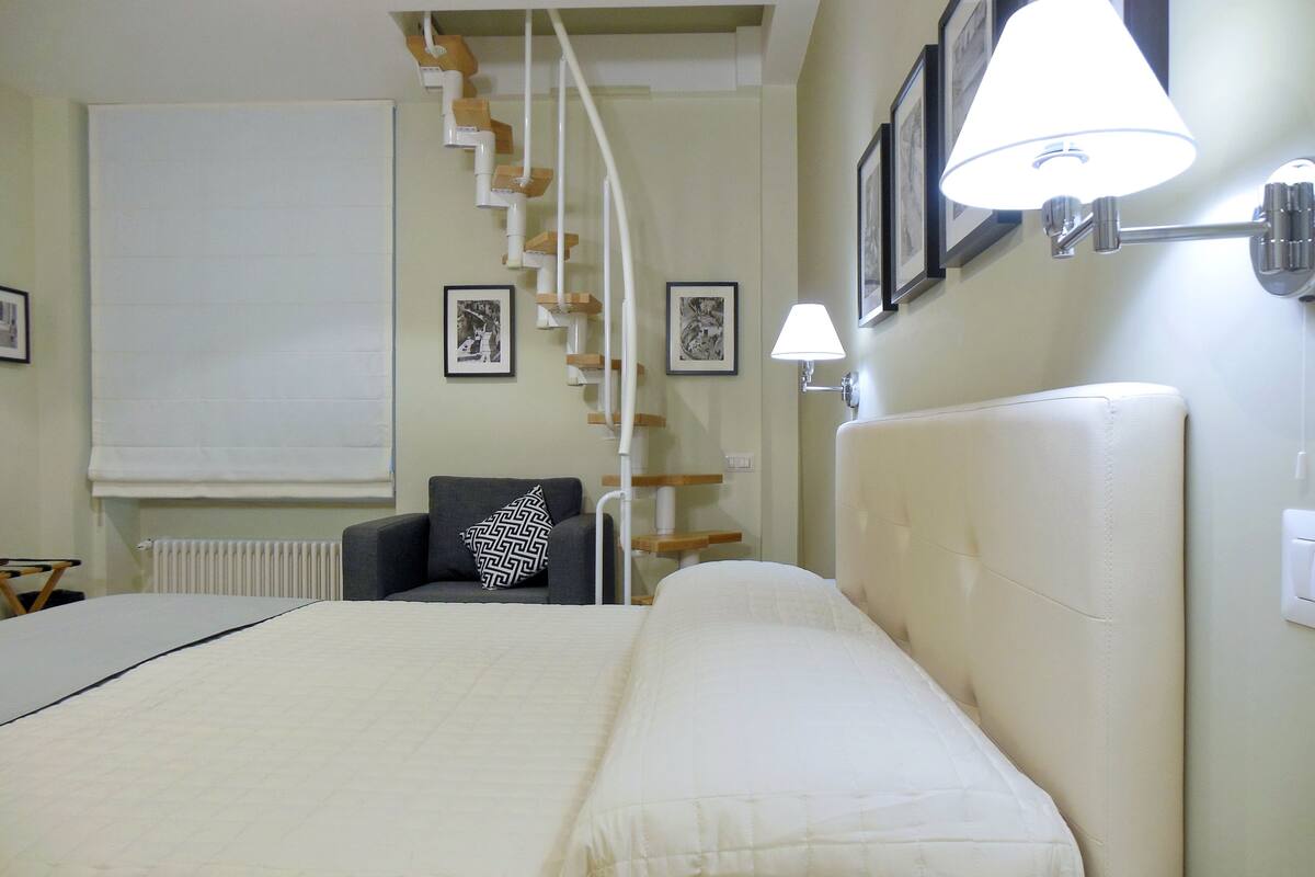 A hotel room with a large bed, a chair, a staircase, and wall-mounted lamps.