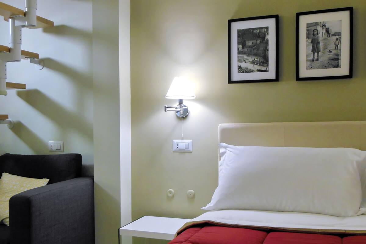 A hotel room with a bed, a nightstand, a lamp, and two framed pictures on the wall.