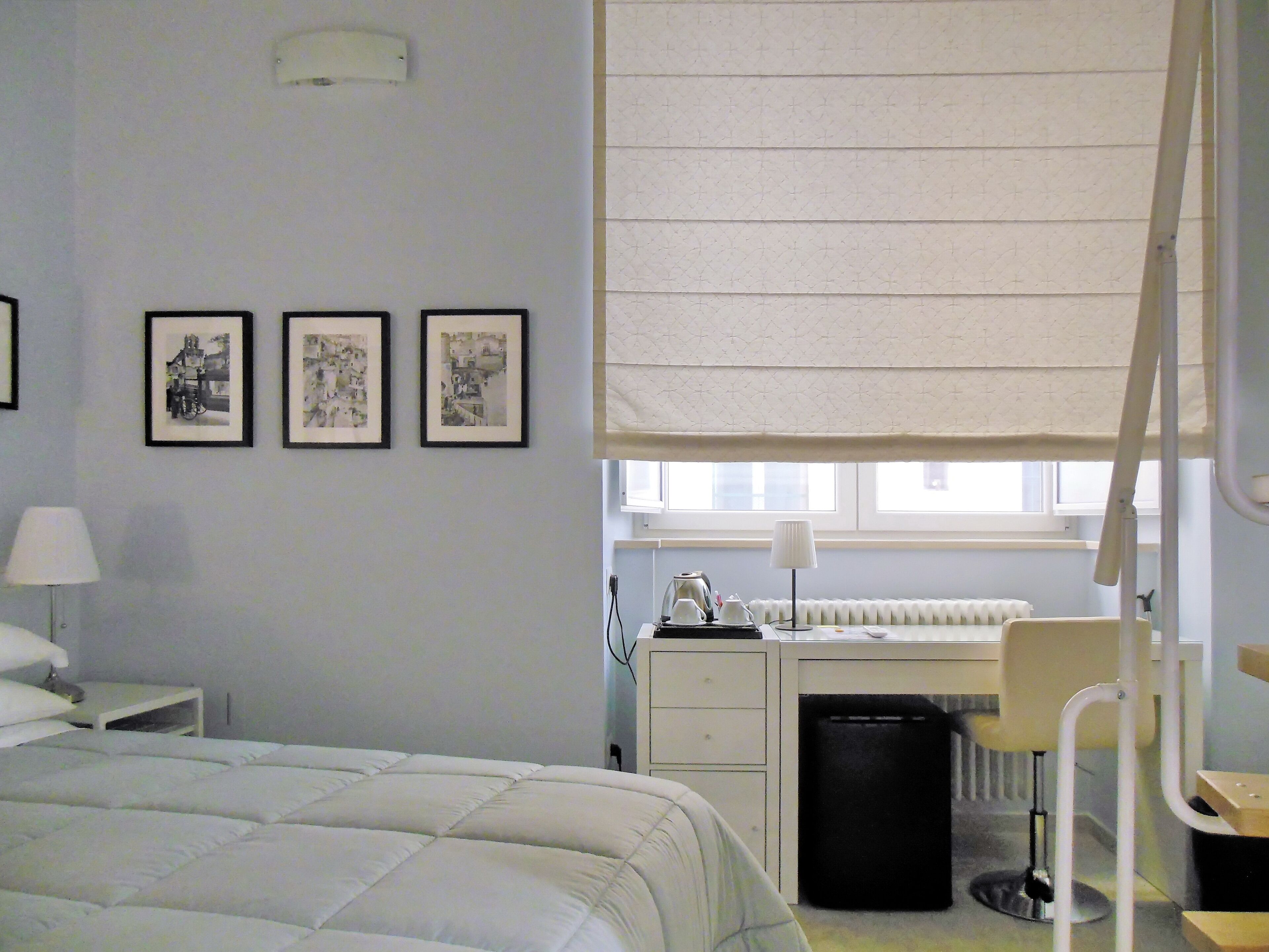 Ein Schlafzimmer mit einem Bett, einem Schreibtisch, einem Stuhl, einer Heizung und einem Fenster mit Jalousie.
