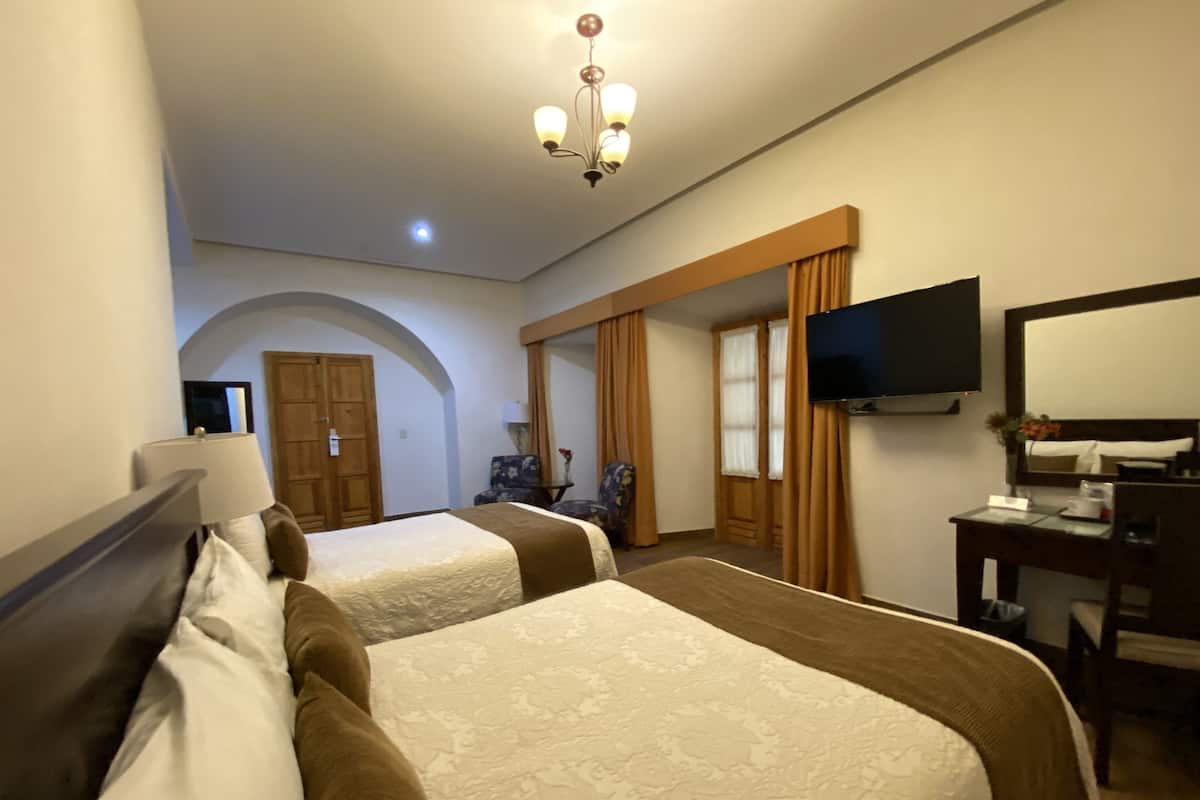 Una habitación de hotel con dos camas, televisión, escritorio con silla y espejo.