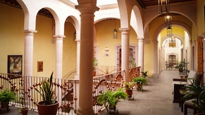 Um pátio interno com arcos, colunas, plantas em vasos e uma escadaria.