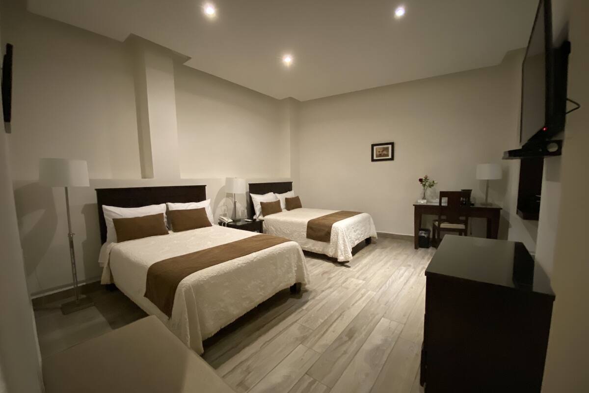 Una habitación de hotel con dos camas, un escritorio, una silla y un televisor.