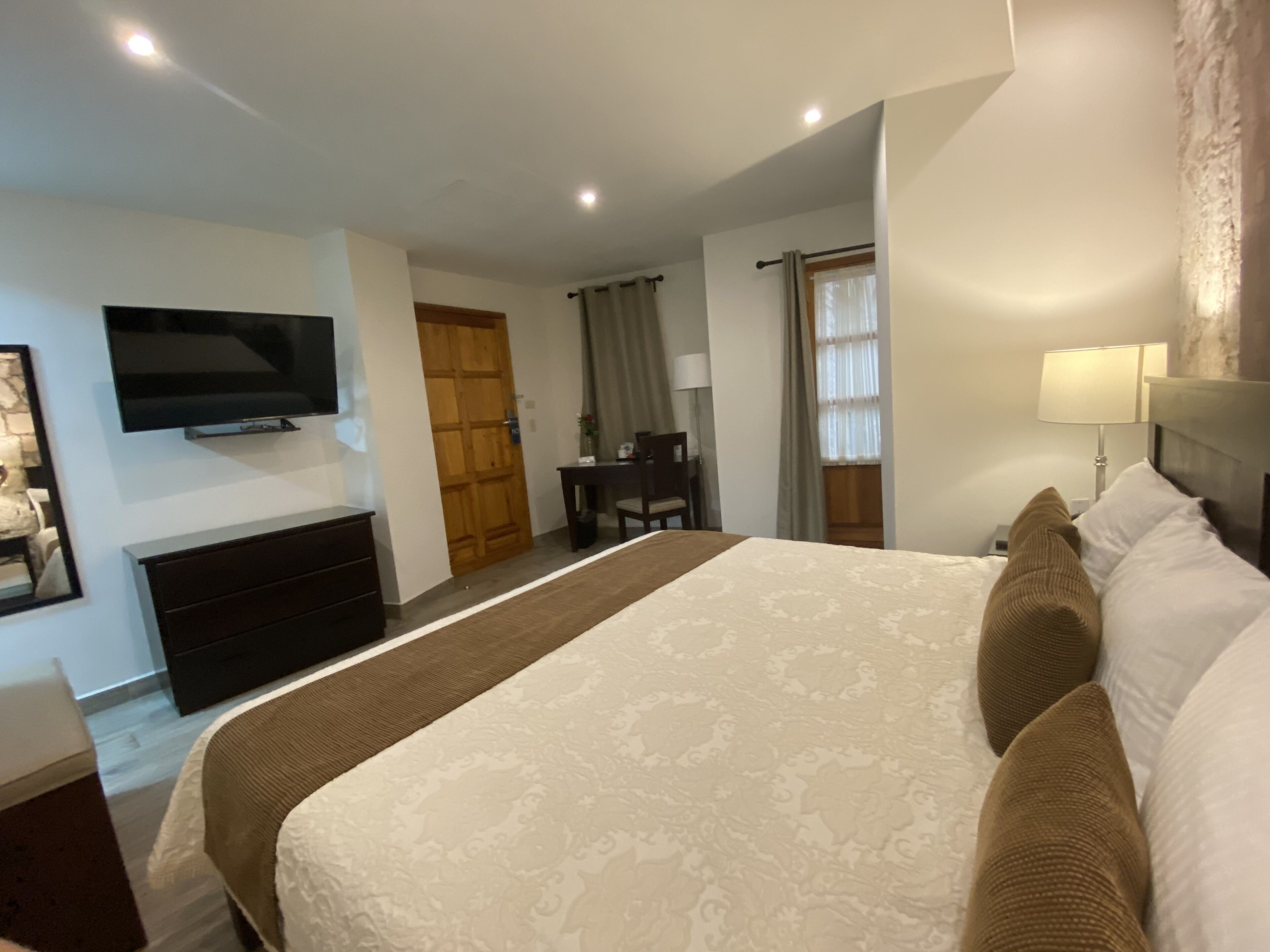 Une chambre d’hôtel avec un grand lit, un téléviseur à écran plat fixé au mur, un bureau avec une chaise et une fenêtre avec des rideaux.