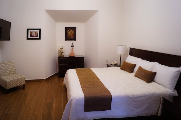 A hotel room with a large bed, a chair, a nightstand, and a lamp.