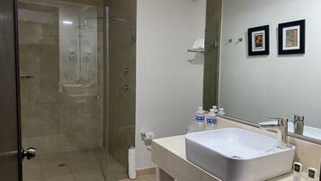 Un bagno moderno con doccia vetro, un lavandino bianco capiente e uno specchio sopra. In evidenza due quadri appesi alla parete.