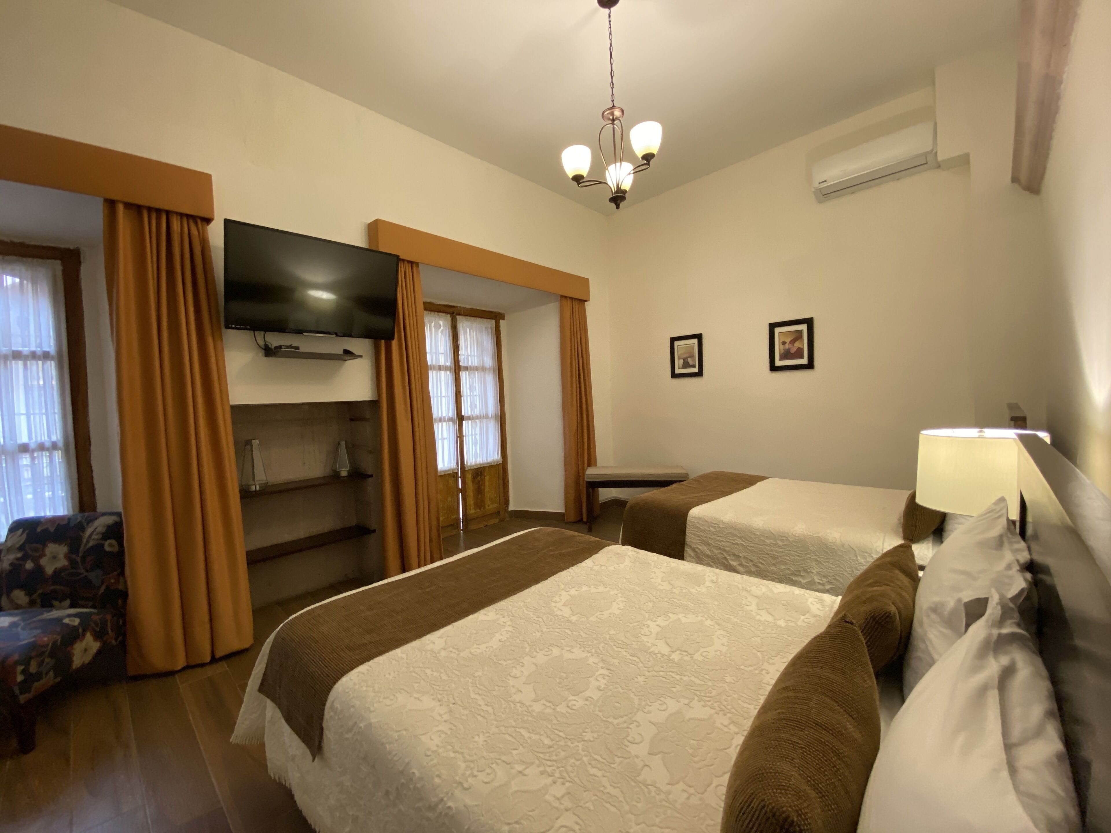 A hotel room with two beds, a TV, a bench, and a lamp.