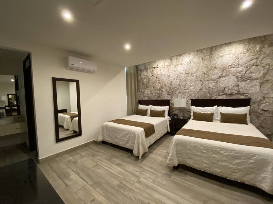 A hotel room with two beds, a stone wall, a mirror, and a wooden floor.