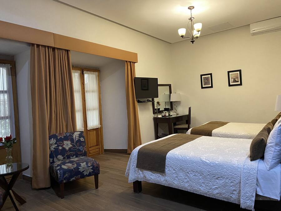 A hotel room with two beds, a desk, a chair, a TV, and a window with curtains.