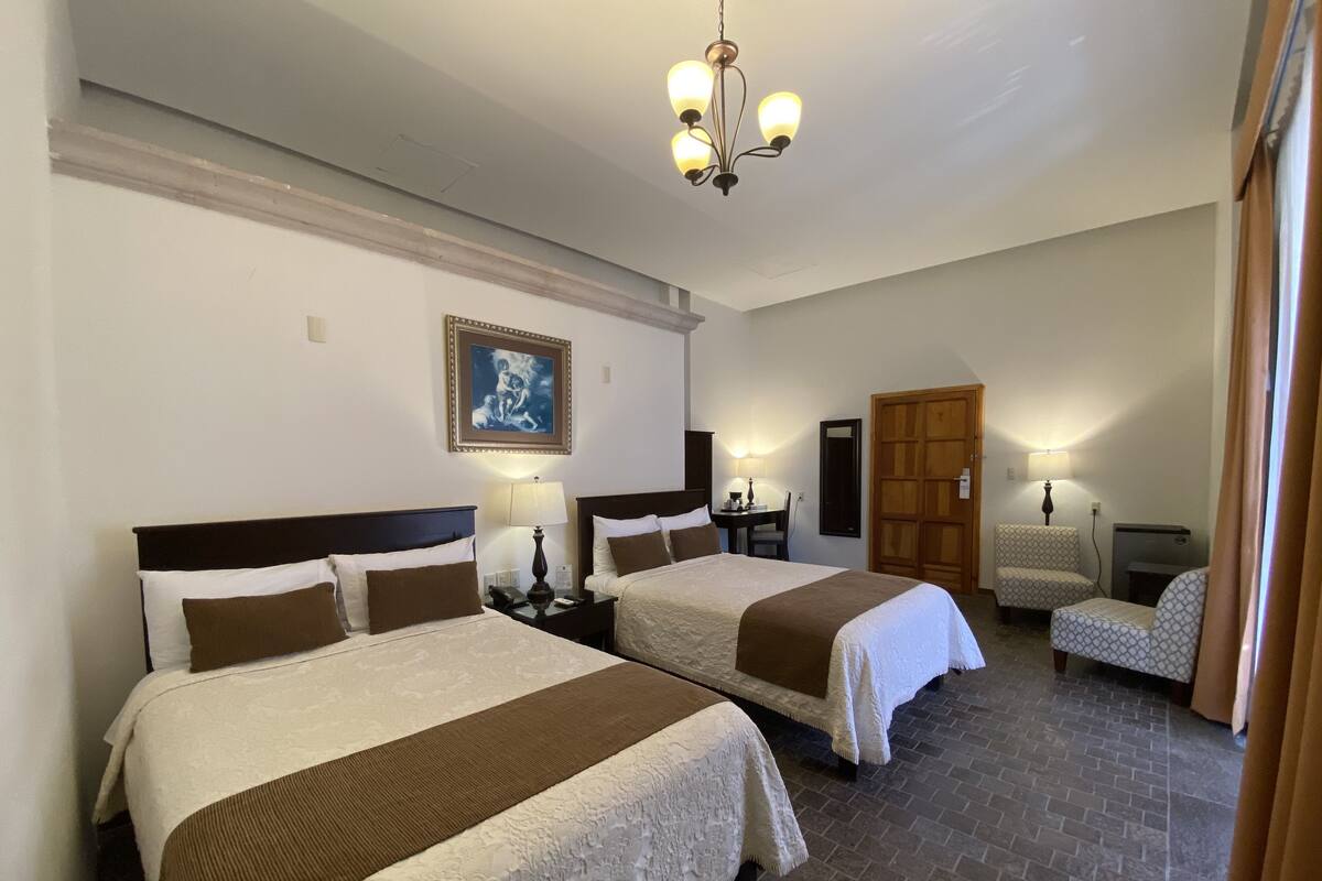 Habitación de hotel con dos camas, un armario de madera, un escritorio con silla y un candelabro.