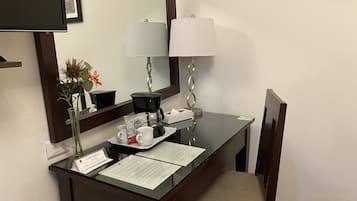 Een bureau in een hotelkamer met een koffiezetapparaat, twee kopjes, een zakdoos en een naambadje.