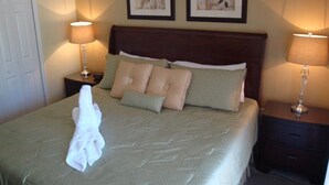 Un lit bien fait, recouvert d’une couvre-lit verte et agrémenté de plusieurs oreillers, deux tableaux floraux encadrés accrochés au mur et deux lampes de chevet.