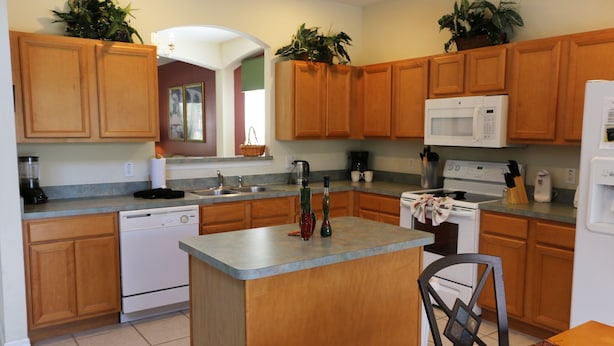 Cocina con armarios de madera, microondas integrado, lavavajillas y una isla central.