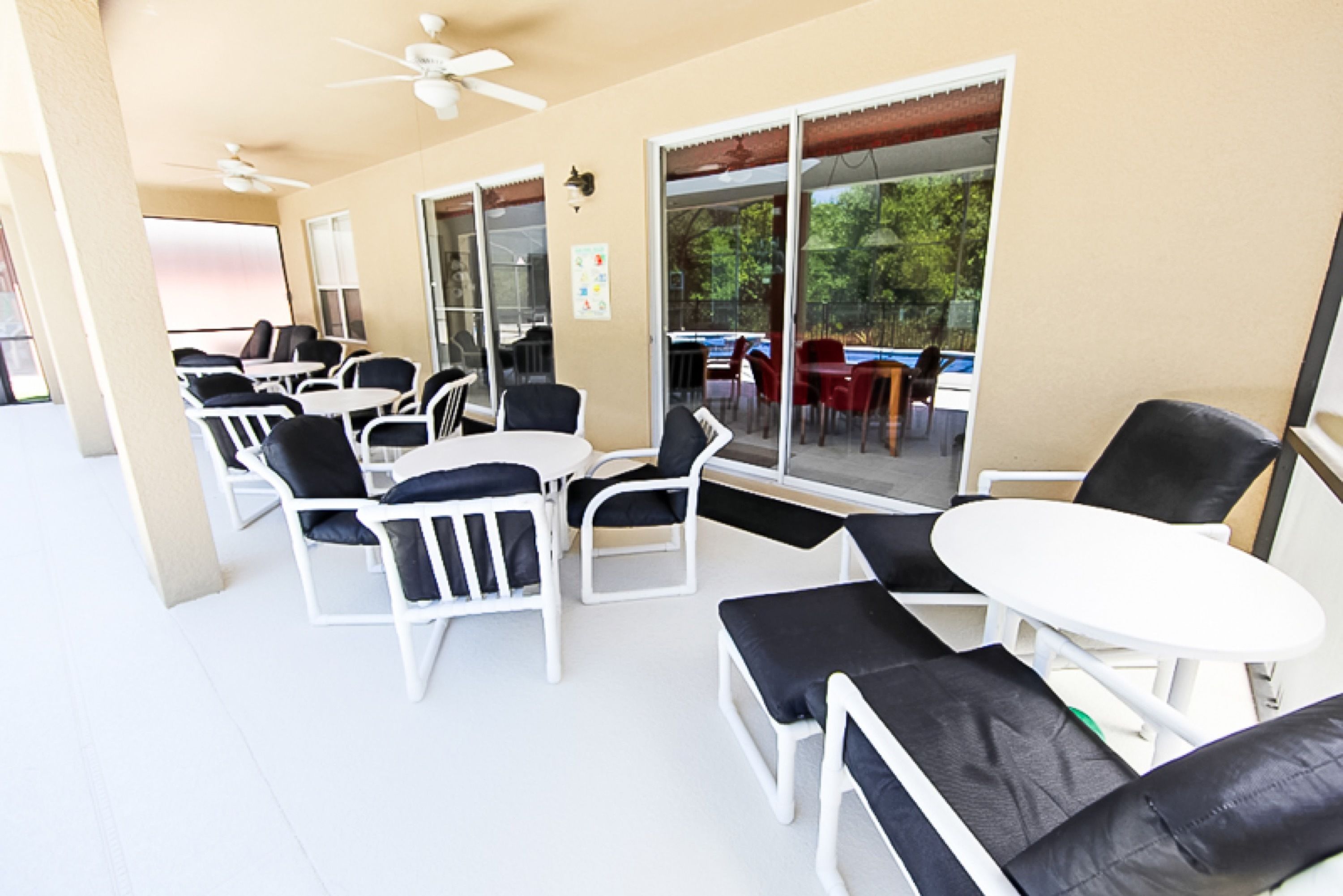 An outdoor patio area with white tables and chairs, a ceiling fan, and a view of the outdoors through large glass doors.