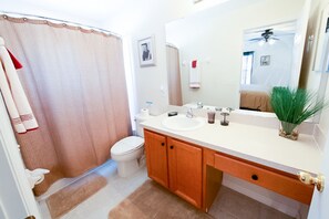 A bathroom with a shower curtain, toilet, sink, and cabinet.