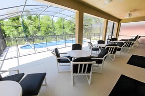A covered outdoor seating area with tables and chairs, overlooking a swimming pool.